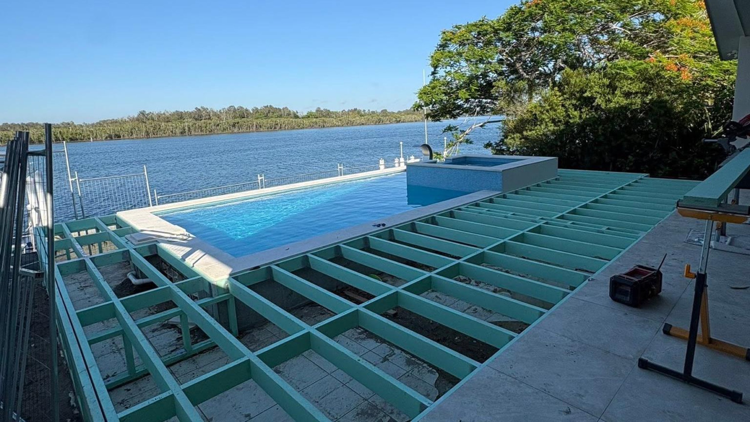 A deck being framed beside a pool overlooking the water