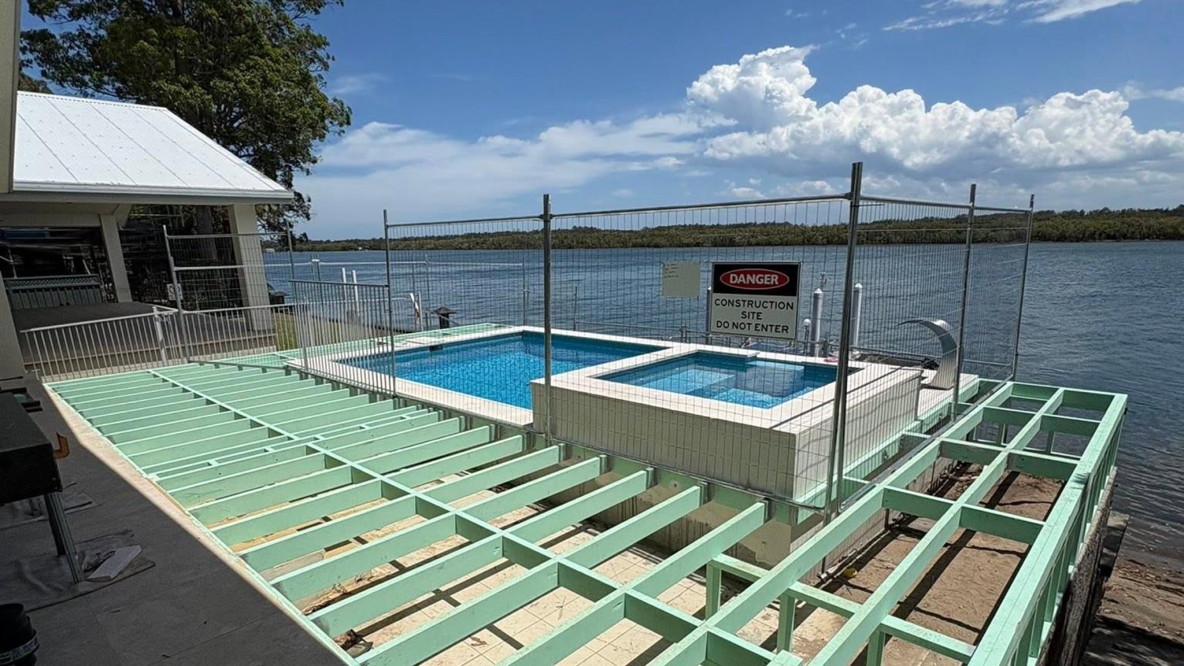 A timber deck frame under construction beside a pool, overlooking the water